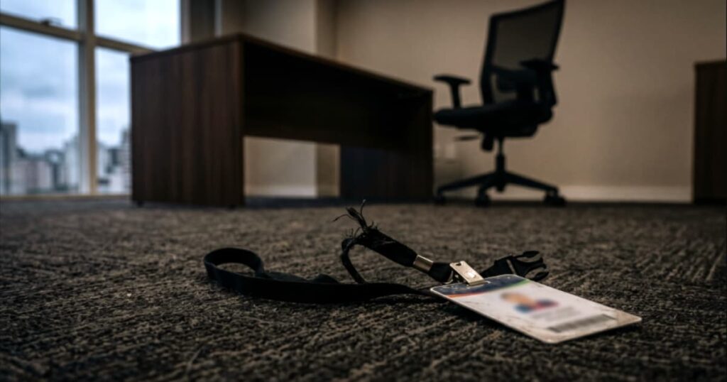 Crachá corporativo jogado no chão ao lado de uma mesa vazia e limpa, ilustrando a demissão e a fuga dos melhores profissionais causada por uma liderança tóxica.