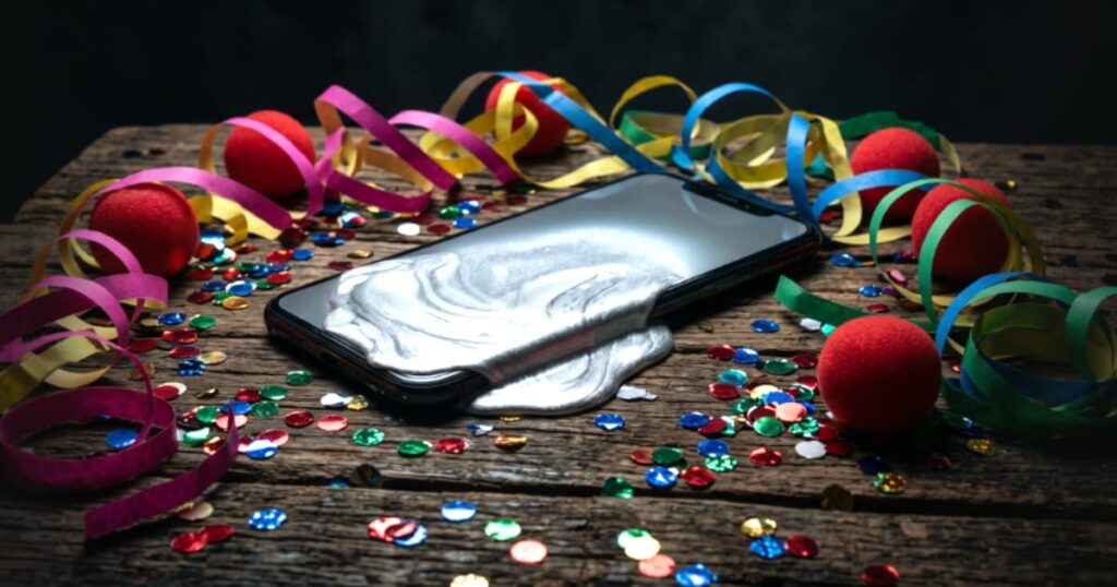 Fotografia conceitual mostrando um smartphone exibindo uma tela de erro derretendo, cercado por confetes de plástico baratos e máscaras coloridas jogadas no chão, simbolizando o desgaste e o fim do circo digital.